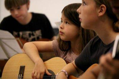 Je ziet twee kinderen kijken naar iemand terwijl ze gitaar les krijgen bij muziekschool Amersfoort
