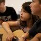 Je ziet twee kinderen kijken naar iemand terwijl ze gitaar les krijgen bij muziekschool Amersfoort